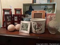 Display of picture frames, spherical candles, ceramic vases and planter, glass container with lid, and mirrored butterfly tray arranged on a wooden surface.
