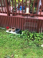 Photo showing all five ceramic flower pots lined up on a white board on grass next to a red wooden fence, with the black wrought iron plant stand and tall candle holder holding a white candle beside them.