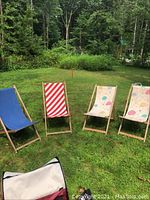 Four wooden frame folding sling chairs set outdoors on grass: one solid blue, one red/white stripes, two matching with leaf and balloon patterns.