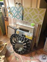 Set of decorative items on floor including three round mirrors with metallic frames, picture frames and wall art leaning against wall