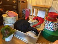 Overall view: multiple hats in plastic bin and four round decorative hat boxes stacked