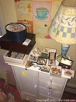 Lot displayed on white cabinet with lamp behind, showing jewelry boxes, earrings, necklaces, watches