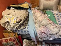 Overview of multiple folded table linens including lace tablecloth and assorted placemats or napkins