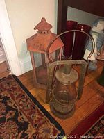 Two railroad lanterns shown on floor, one circular metal with glass (antique), and one red with peaked roof design