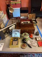 Wide view of vintage items on table including wooden boxes, photo albums, Coronet radio box, and various small vintage objects