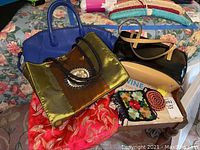 Photo showing a blue leather handbag, gold and brown tote bag with embroidery, black and tan purse, and small fabric and crocheted change purses on a floral bedspread.