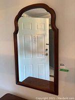 Front and side views of a rectangular wall mirror with a wooden frame and a decorative arched top edge, showcasing reflections of room elements like a door and kitchen.