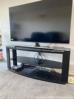 Front view of black metal TV stand with a large flat-screen TV on top and electronic devices on lower shelves, showing overall condition and usage.