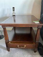 Dark wooden square side table with single drawer, brass handles, lower open shelf, and paneled top. Table measures approximately 21x26x20 inches.