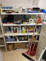 Full view of metal shelves with various cleaning supplies and tools arranged including paper towel rolls, bottles of cleaning liquids, boxes, and hand tools.