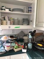 Photo showing the kitchen counter and shelves with kitchen items: Black and Decker citrus juicer, small blender, various cookie sheets, oven mitts, cutlery, mugs, glasses, dishes, and bowls.