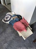 Full lot showing various folded table linens including a crocheted table cloth with embroidered cover, blue and rose linen cloths, pink round placemats, multi-colored placemats in a holder, and quilted protector.