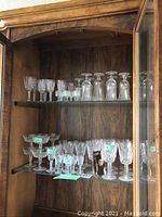 Wooden display cabinet shelf with assorted Waterford crystal stemware including tall water goblets, wine glasses and smaller dessert and cordial glasses.