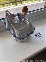 Full view of Royal Doulton Pamela figurine standing on a windowsill, showing the flowing white and blue dress and red hair details.