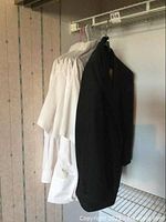 Tuxedo jacket and shirts hanging in closet. Jacket is black, shirts are white, showing 2 long sleeve and 3 short sleeve shirts.