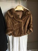 Front view of the brown mink fur stole hanging on a Gourdier branded hanger, showing the short-length design and texture of the fur.