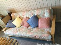 Full front view of wood frame futon with cushions and five colorful throw pillows.