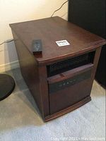Dark wood finish electric room heater on carpeted floor, control panel visible with icons, remote placed on top.