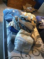Photo showing bedding items spread on bed: electric blanket, mattress cover, sheets, and some cables for electric blanket.