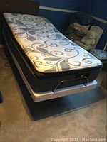 View of the twin mattress and adjustable metal power lift bed frame in a bedroom setting.