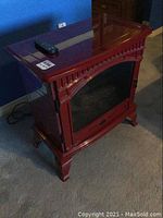 Red Dimplex electric fireplace with wooden cabinet frame and remote control on top.