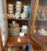 Photo of china cabinet with stacks of plates, cups, and serving dishes.