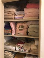 Photo showing shelves filled with folded towels in beige, pink, gray colors; pillows and possibly an electric blanket packed in plastic bag