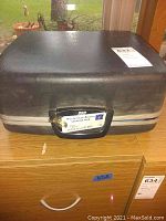 Closed black carrying case with a handle and metal trim, placed on a wooden surface.