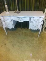 Full front view of the white painted vintage style wooden desk with five drawers closed. Shows the curved legs and decorative drawer fronts.