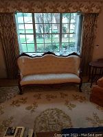 Front view of vintage tufted back couch placed in front of large window, showing carved wood frame and fabric upholstery.