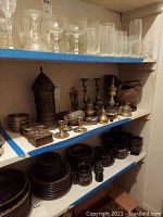 Photo displaying multiple brass candleholders, trinket boxes, a pierced tall lantern, and other brass items arranged on shelves.
