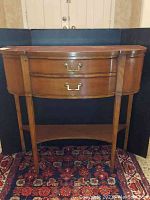 Front view of wooden console table showing two drawers with brass handles, curved front, straight legs, and bottom shelf. Surface shows wear and scratches.