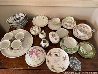 Overview of assorted porcelain teacups, saucers, bowls, platters, and decorative boxes arranged on table.