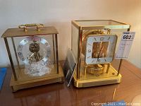Two brass and glass clocks side by side (Kundo on left, Jaeger-LeCoultre Atmos on right)