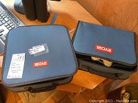 Two blue padded Ryobi branded carrying cases containing the drills and accessories.