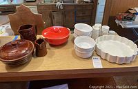View of full lot including brown lidded casserole, red casserole with lid, two brown Marcrest pitchers, multiple white casserole dishes and condiment cups.