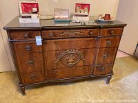 Front view of wooden dresser showing ornate carved drawer fronts, metal round pulls, and a glass top surface with various small boxes on top.