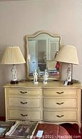 Full front view of cream dresser with mirror, showing six drawers and two lamps on top.