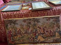 Six pieces of wall art laid on a patterned fabric surface including a large tapestry and framed prints