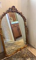 Full view of the large framed mirror showing overall shape and decorative frame with gold floral scroll details.