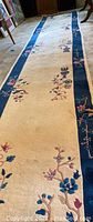 Full length view of beige rug runner with blue floral borders on carpeted floor.