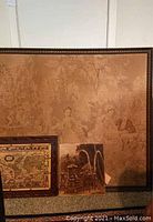 Large classical style fabric wall art with faint human figures and trees in monochrome sepia tones, accompanied by two smaller artworks leaning against it.