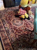 Burgundy Oriental-style area rug with floral medallion pattern and fringe under stuffed animals