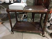 Wooden rolling cart shown from side view with white desk safe on top shelf and lower storage shelf visible