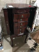 Front view showing six drawers with round metal handles and side doors on a wooden jewelry chest with carved wood detail.