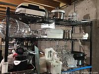 Wide view of three shelves containing multiple kitchen appliances and glassware.