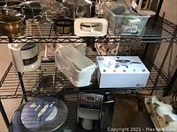 Three shelving units filled with various kitchen appliances and tools including a Cuisinart coffee maker, white bagel slicer holder, and boxed kitchen gadget.