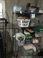 Metal shelving unit loaded with bins, laundry basket, folded fabric, and various storage totes containing sewing and craft supplies