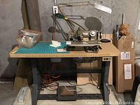 Full view of vintage industrial sewing machine on a sturdy table with attached lamps and foot pedal.