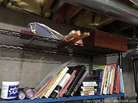 Shelf with various books, some stacked and some leaning, presence of art supplies and a container labeled YES! Gel Medium